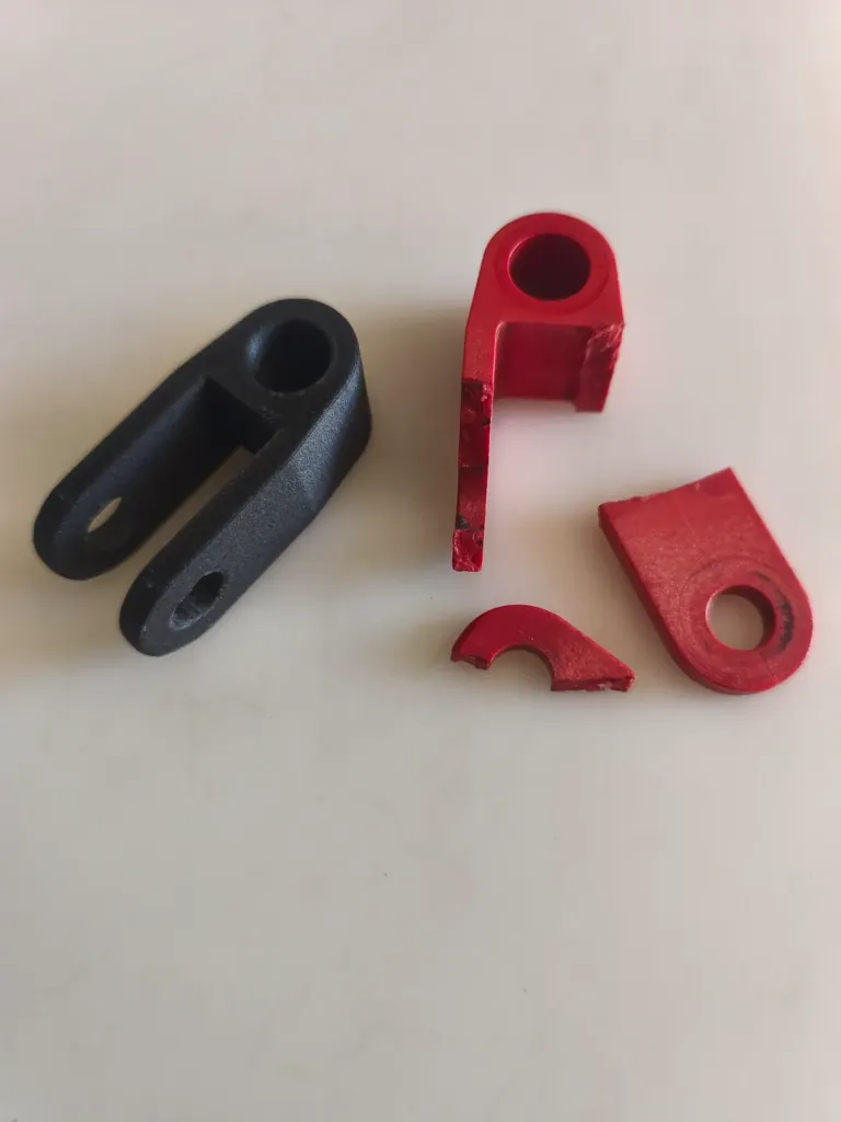 Pièce plastique rouge cassée à côté de sa copie noire refabriquée en impression 3D