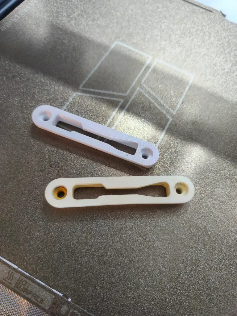 Pièce d’origine jaunie et sa copie blanche imprimée en 3D, sur le plateau de l’imprimante